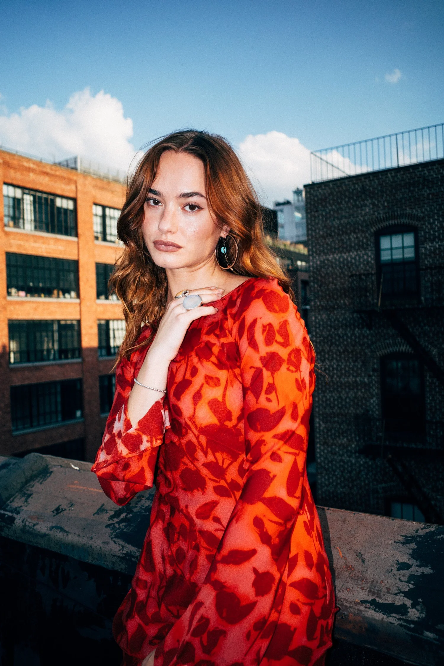 Johnny wearing a red patterned dress on a rooftop beneath a blue sky