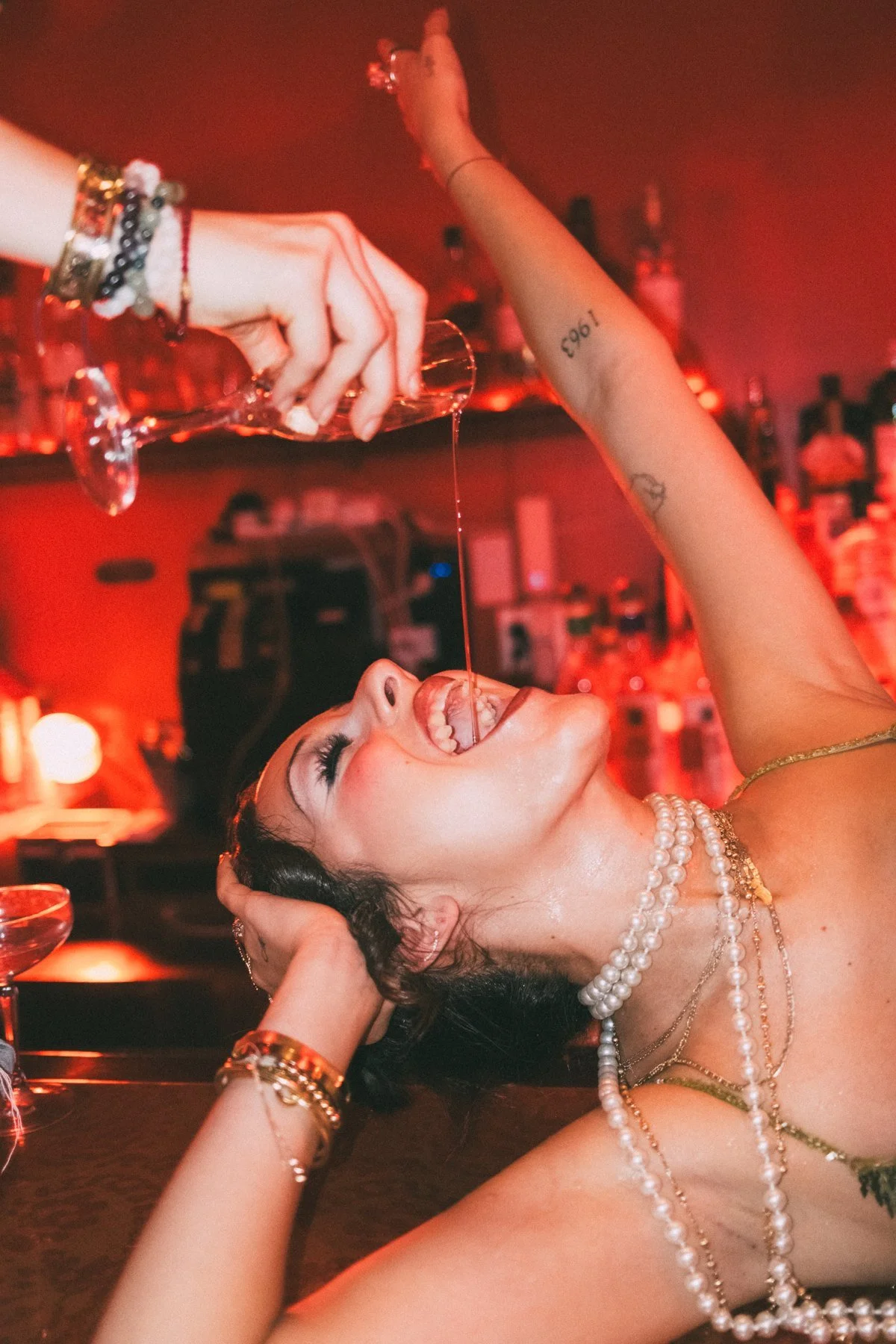 Eden reclining on the bar with her face tilted upward and one arm extended