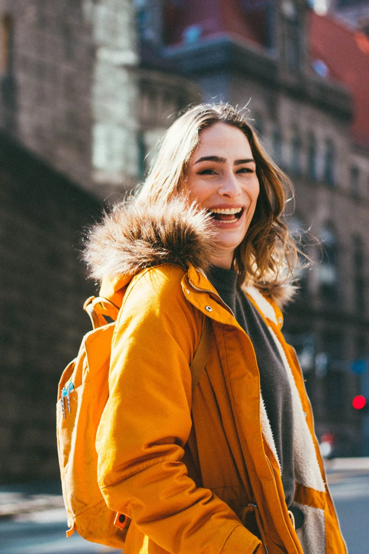 Sarah smiling in a yellow coat with a textured hood and gray sweater