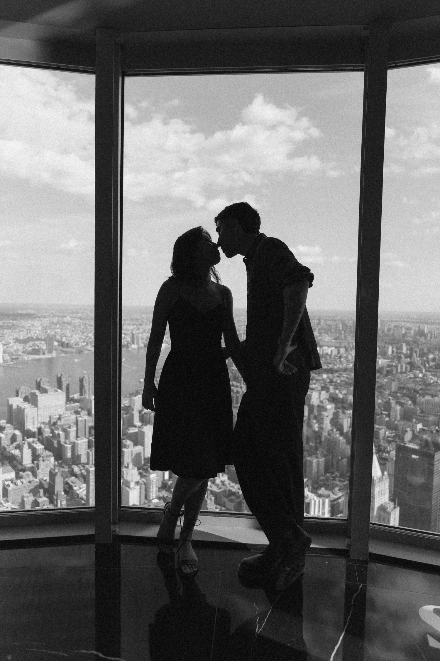 Black-and-white silhouette of Sophia and Mike kissing in front of a tall window overlooking the city