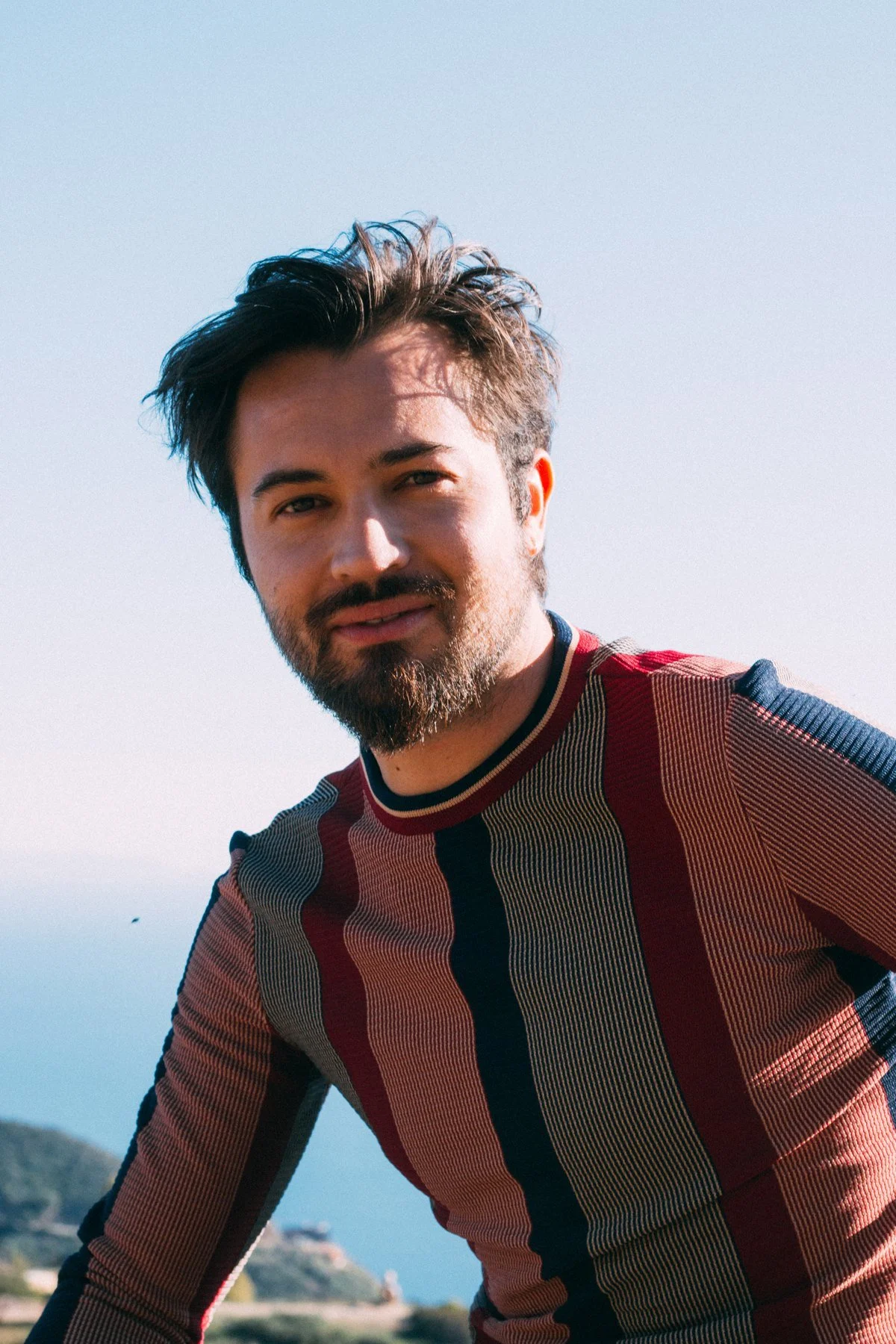 Taylor in a striped knit shirt against a pale blue sky