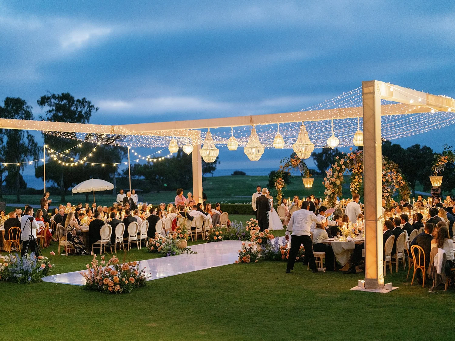 Beaded chandeliers suspended from H-truss above a blue-hour wedding reception at The Lodge at Torrey Pines