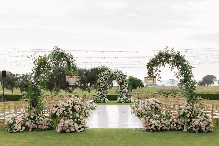 Daytime wedding ceremony with floral arches and cafe-light canopy at The Lodge at Torrey Pines