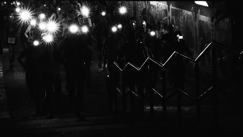 A line of runners at a night-time race start, head torches lit