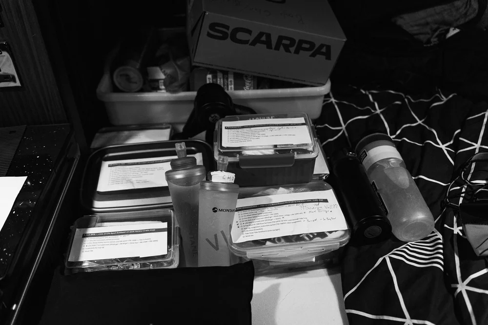 Crew boxes at an ultramarathon checkpoint with the written fuelling plan taped to each lid and soft flasks ready
