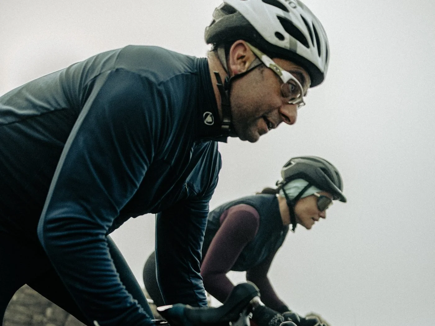 Dr Howard Hurst and Dr Liz Mahon close together on their road bikes on a misty climb