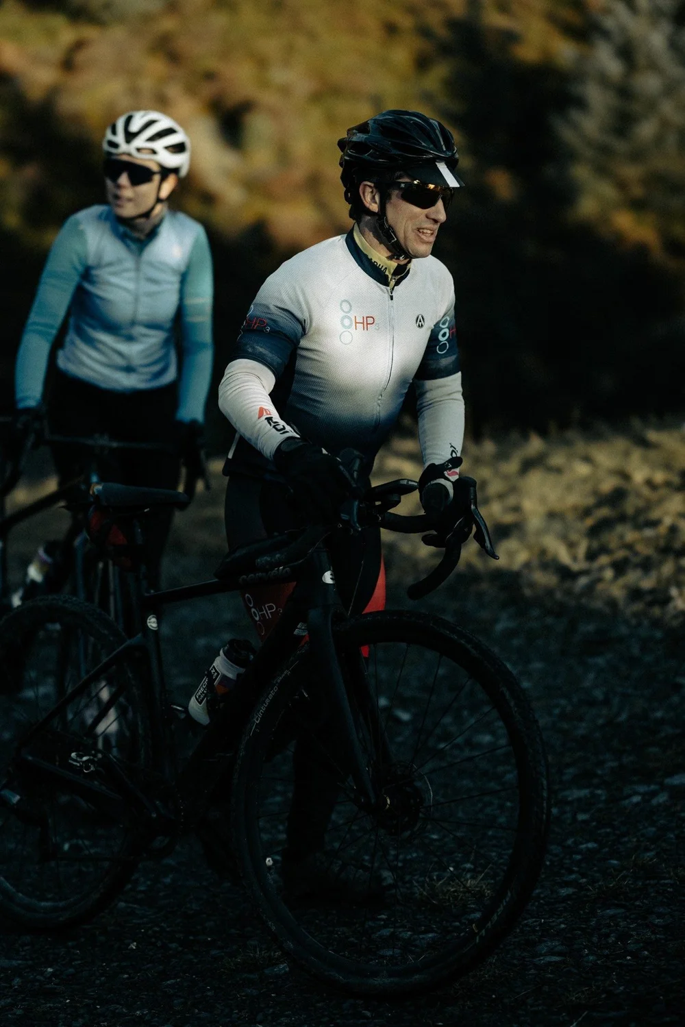 An HP3 coach in team kit riding a gravel bike with Dr Amy Whitehead following behind