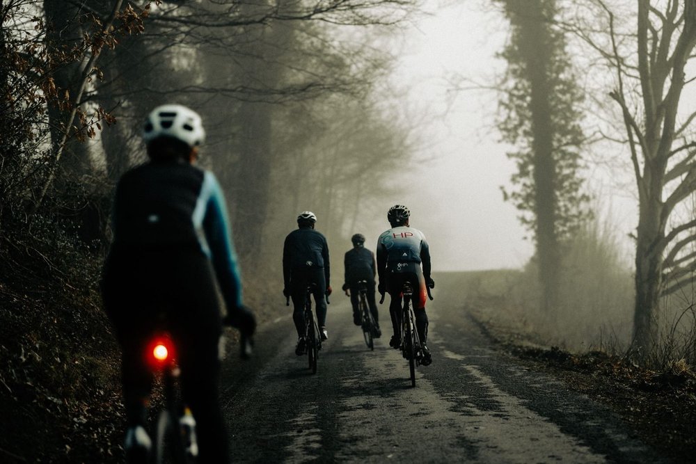 Four cyclists riding away up a misty tree-lined lane, one in HP3 team kit