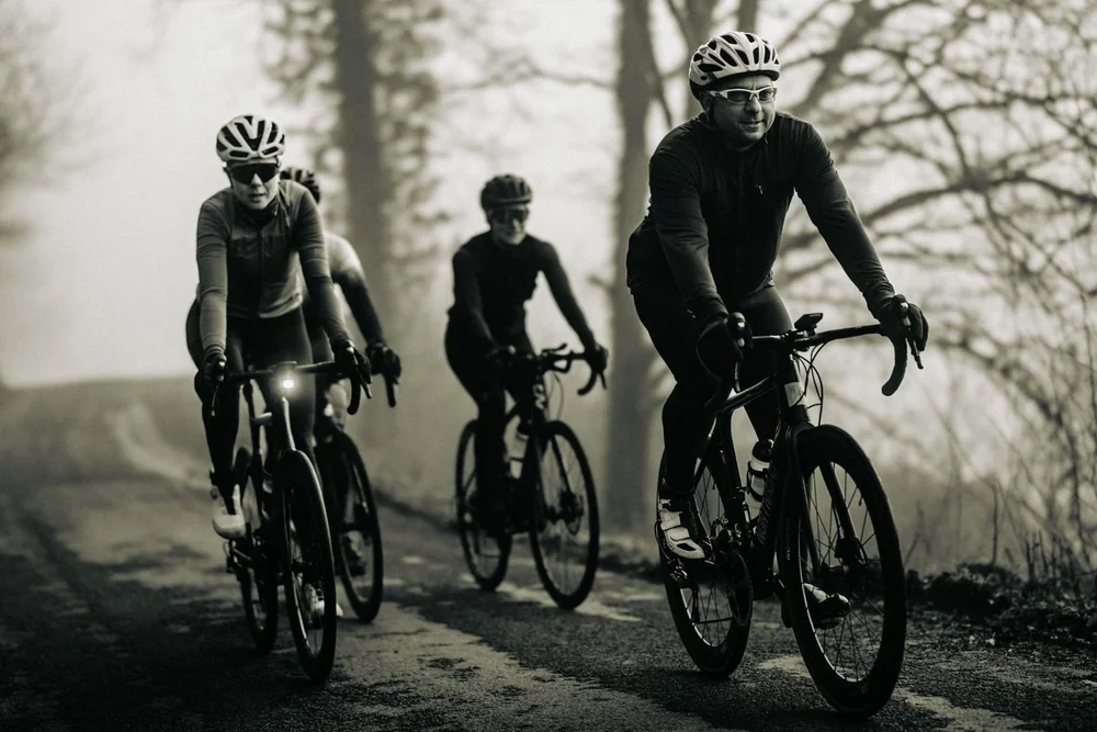 A group of road cyclists climbing through thick fog, photographed in black and white, Dr Amy Whitehead at the front