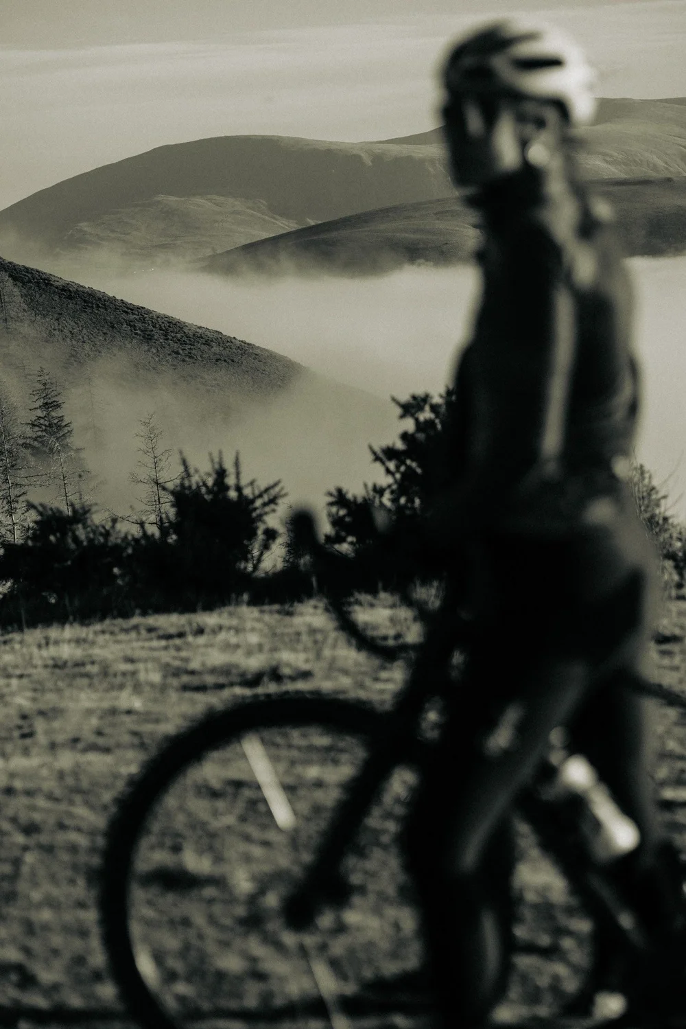 A cyclist in soft focus in the foreground, looking out over fells rising above a cloud inversion