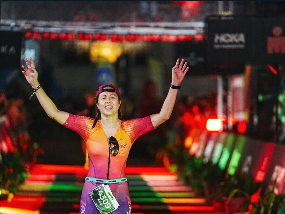 An athlete crossing the Ironman Portugal finish line at night, arms raised