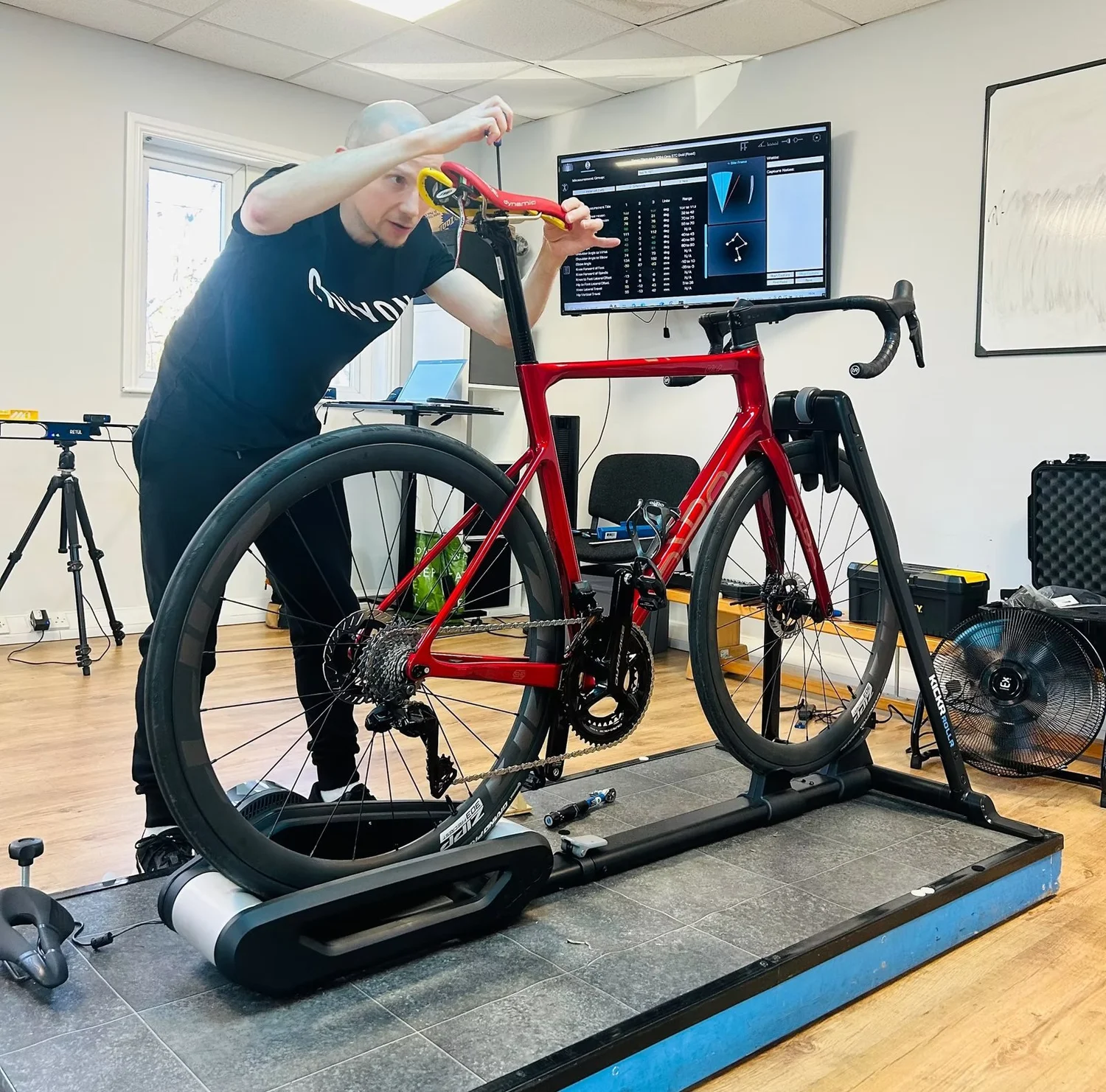 A rider on the fitting jig in the HP3 lab, with motion-capture data on the screen behind
