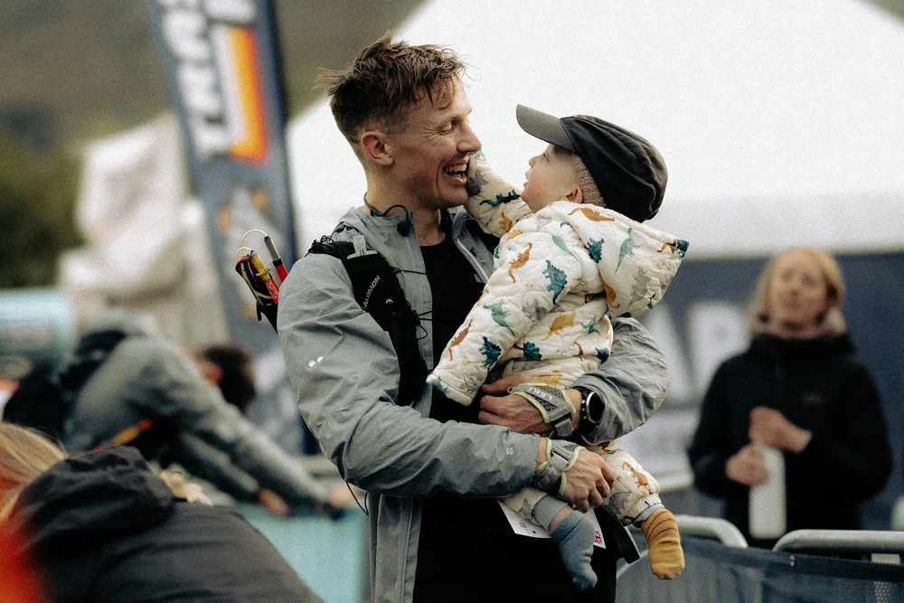 An HP3 athlete laughing with his baby in his arms at a race finish