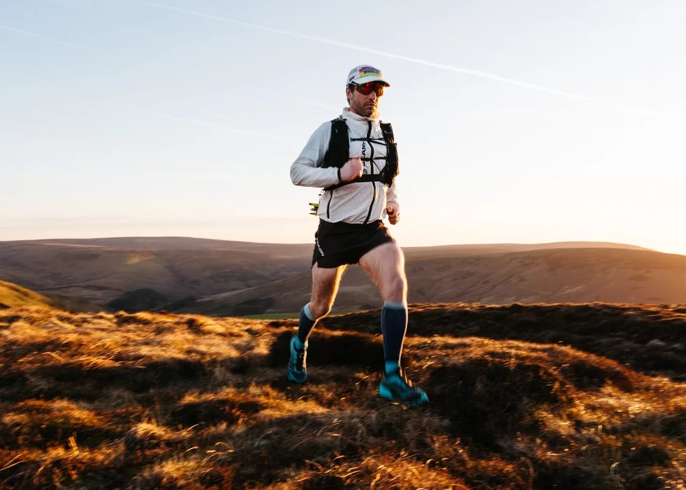 A trail runner crossing open moorland with the sun setting behind him