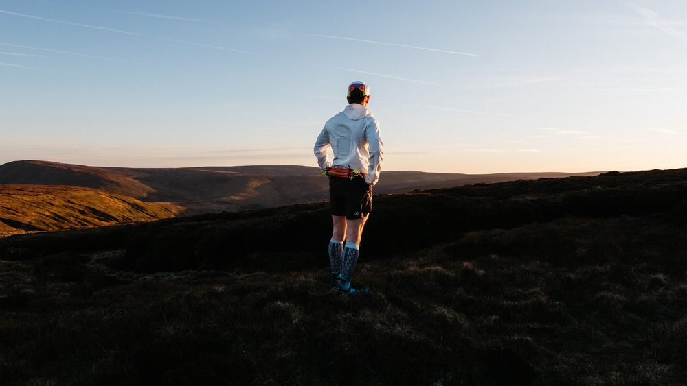 A lone trail runner on a moorland horizon at dusk