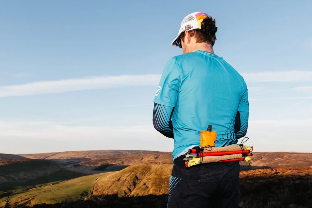 A trail runner seen from behind, soft flasks and gels in the belt, moorland beyond