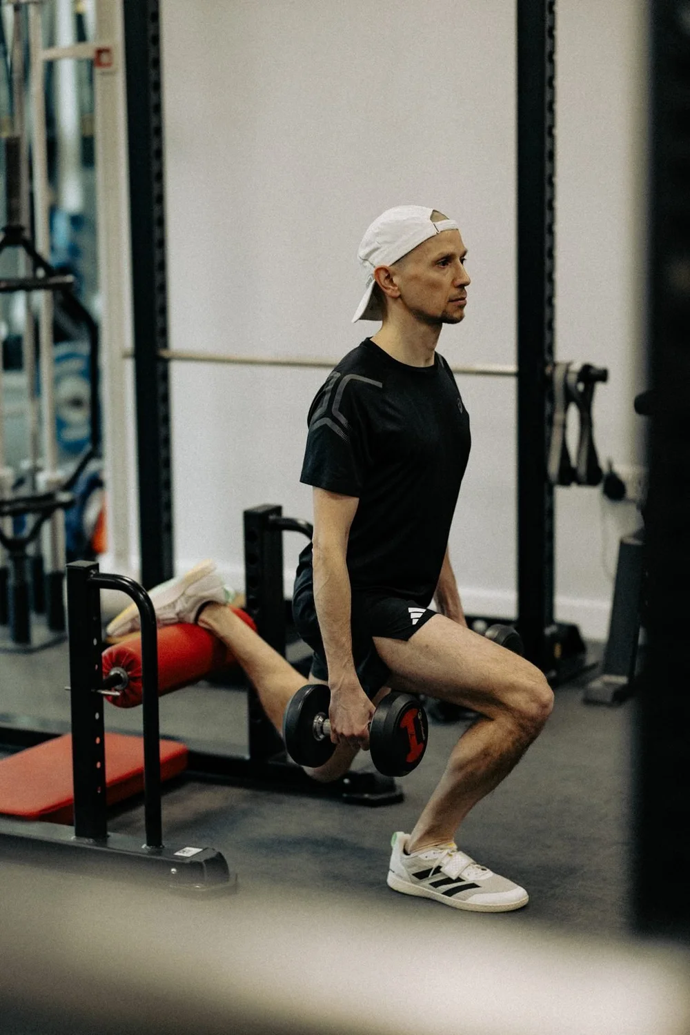 An athlete performing a rear-foot-elevated split squat with dumbbells