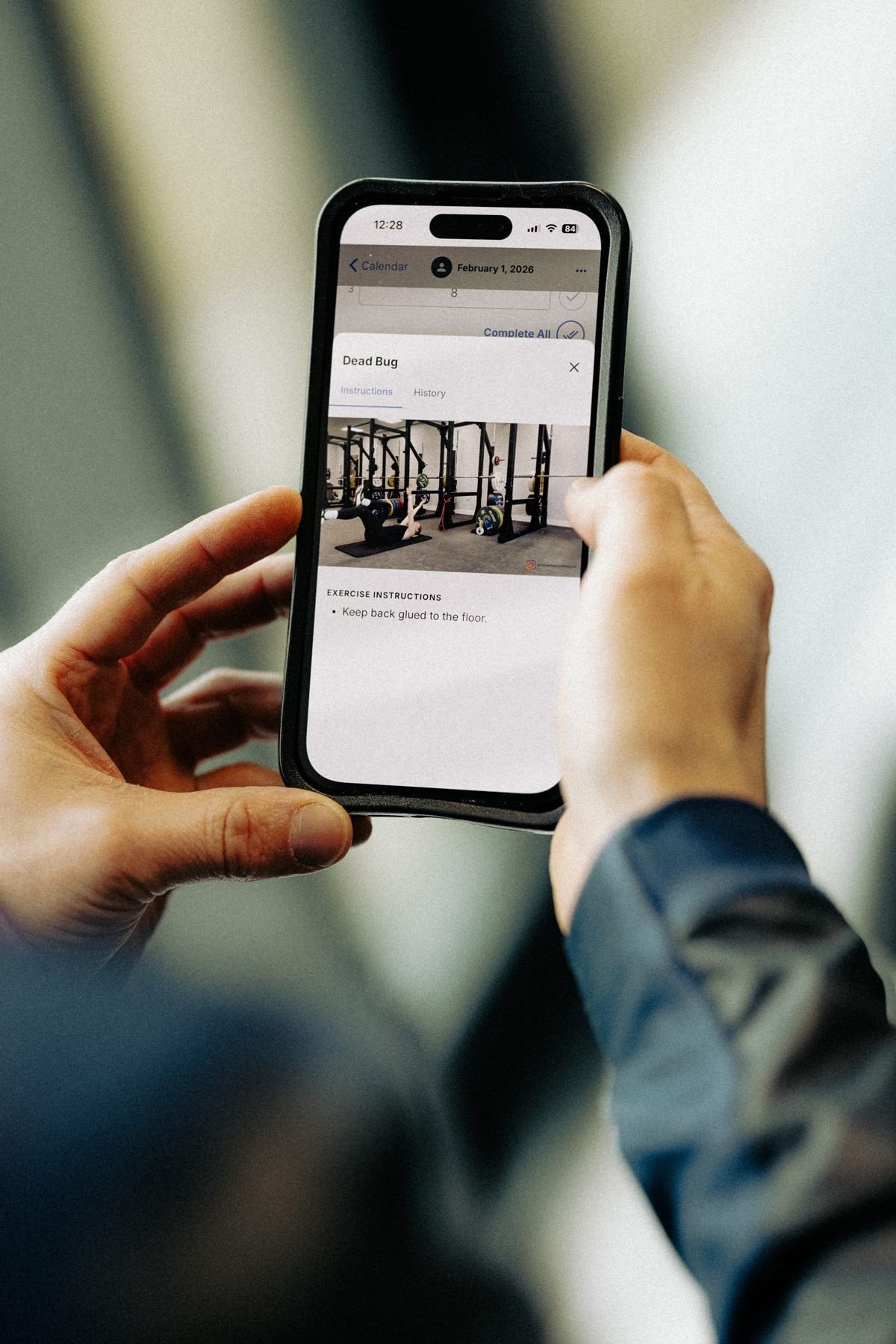 An athlete holding a phone open on a planned strength session in the TrainingPeaks app, with an exercise video and instructions