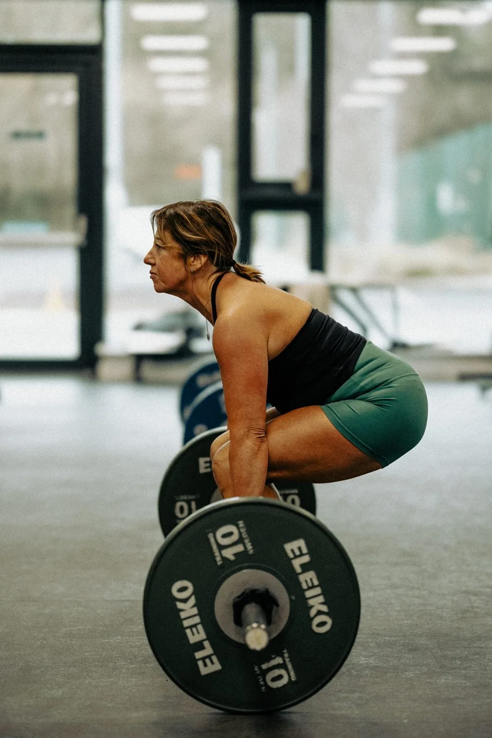 An athlete at the bottom of a barbell deadlift, back flat and bar at the shins