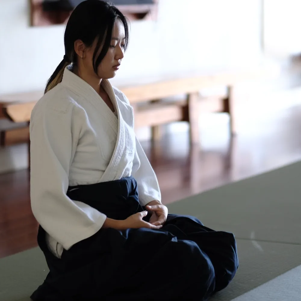 A Budo Scholar student kneeling in seiza on the tatami, eyes closed, hands resting in her lap