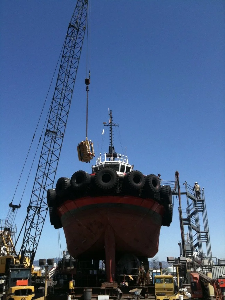 Crane lifting a new engine into a tug in drydock
