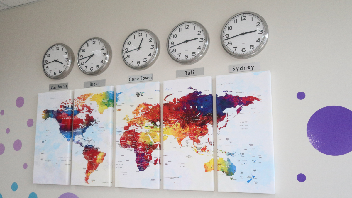 Multiple time zones represented by analog clocks and colorful maps displayed on office wall