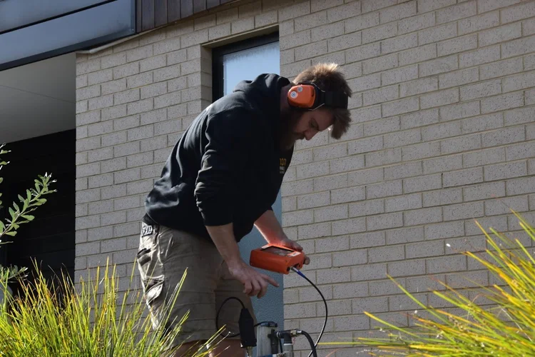 1300 FINDLEAK technician using an acoustic ground microphone to listen for an underground water leak outside a Melbourne townhouse