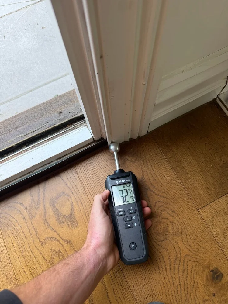 Moisture meter reading the timber floor beside a balcony sliding door in a Cremorne home
