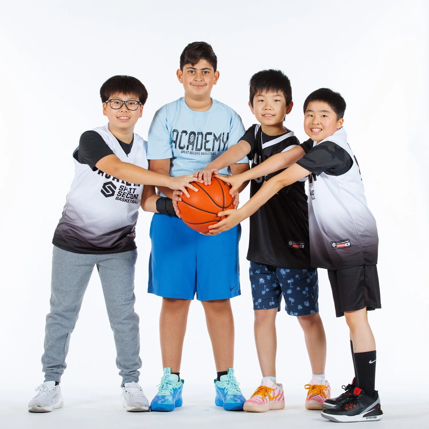 Four Academy players with their hands on one basketball