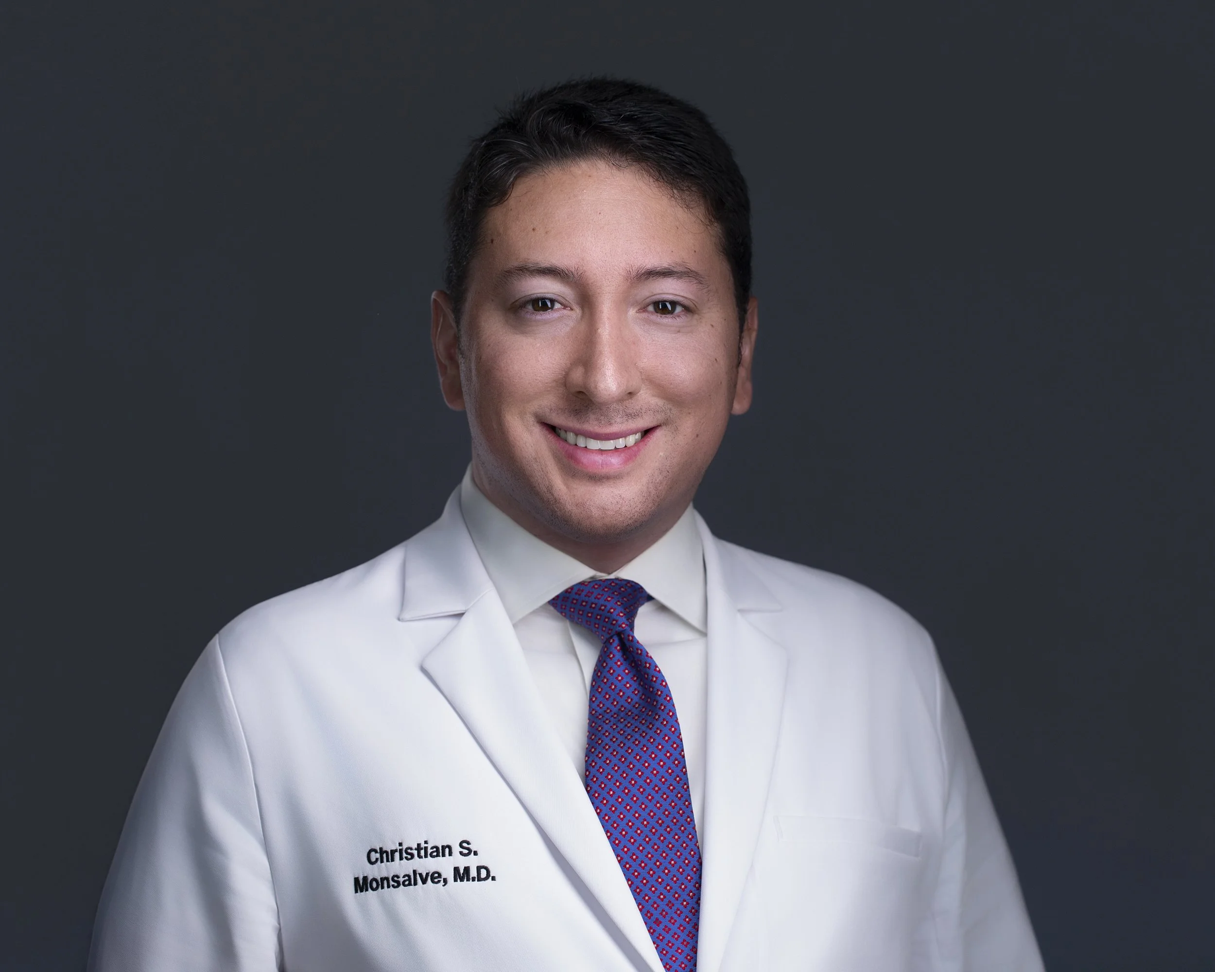 Studio headshot of Cristian wearing a white medical coat