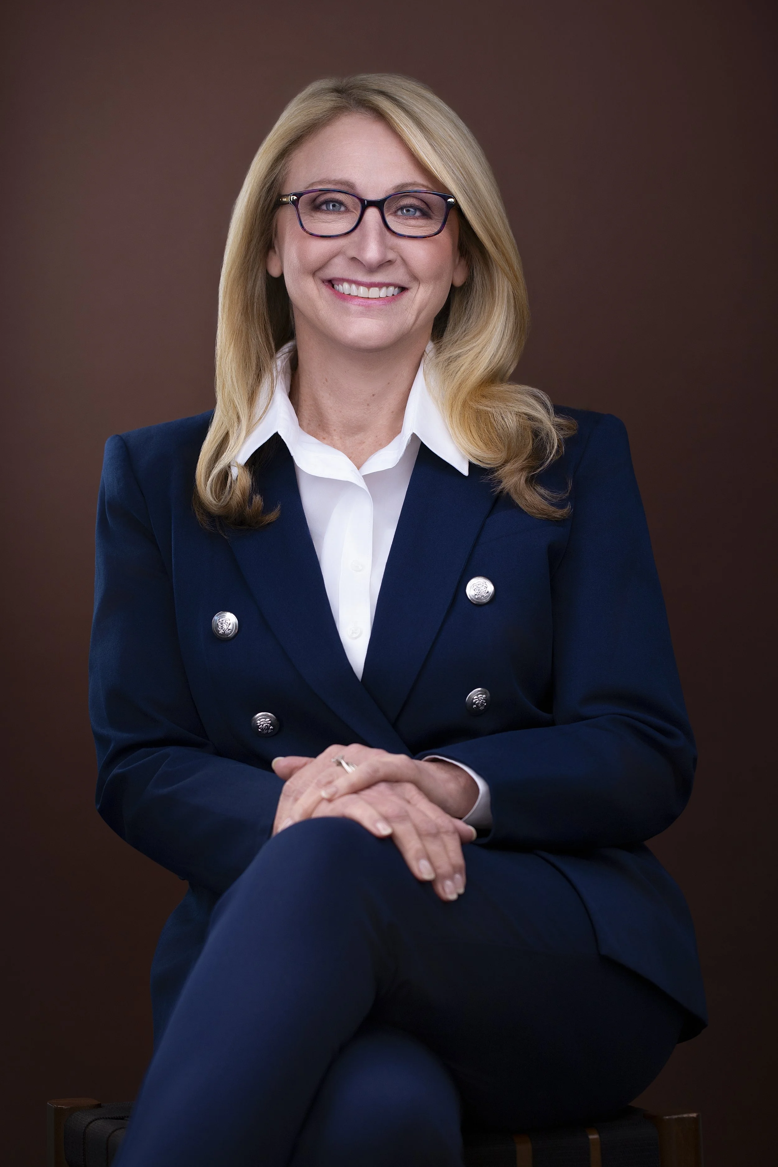 Seated portrait of Michelle wearing a navy suit against a warm brown background