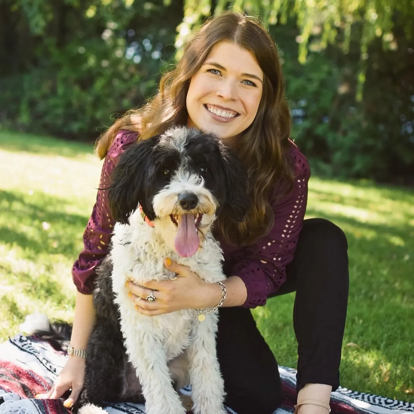 Korie Boyle, On the Mark Balanced Training assistant trainer, sitting outside with a happy bernedoodle on a sunny day in the Pacific Northwest.