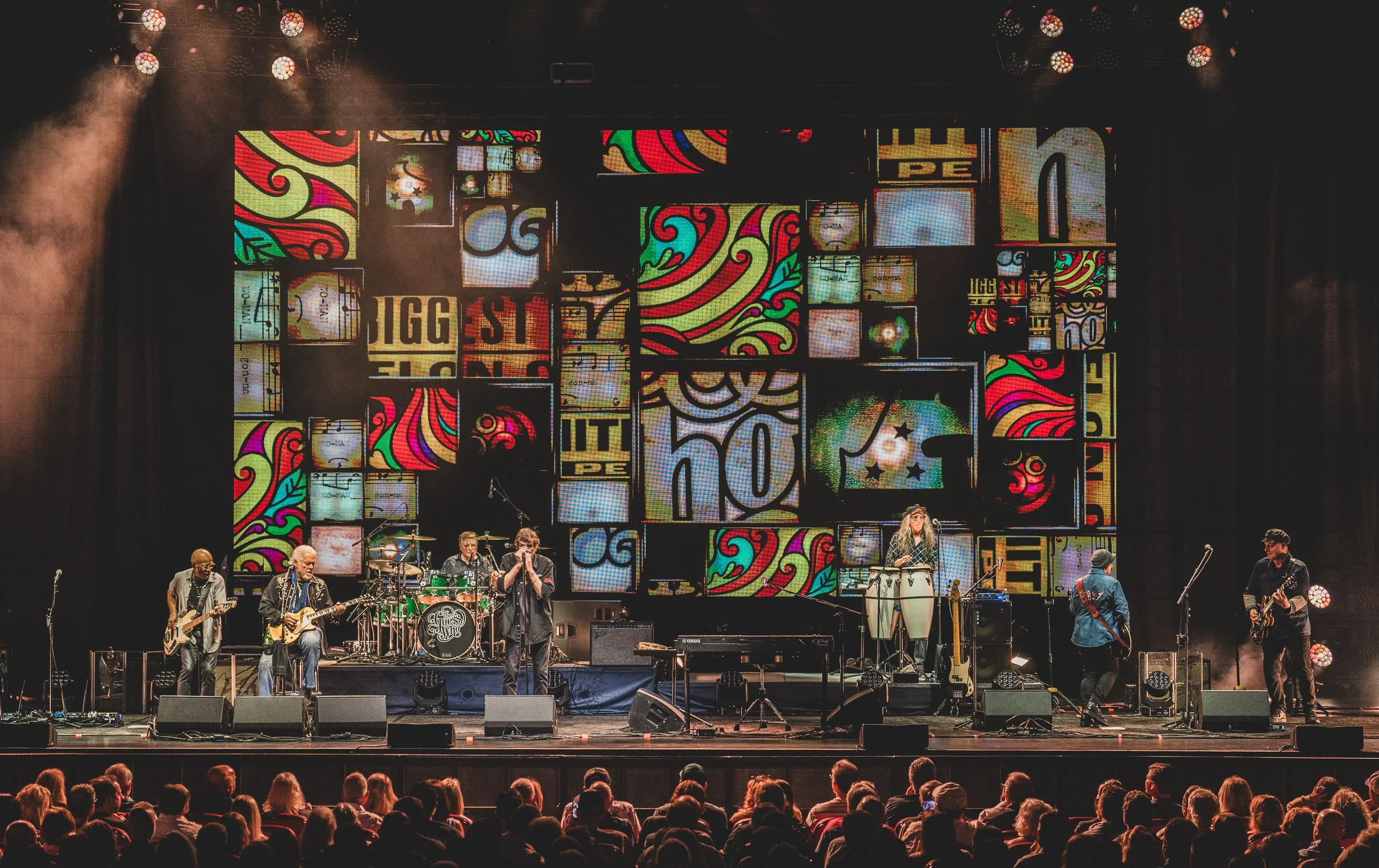 The Guess Who on stage with a colourful concert backdrop