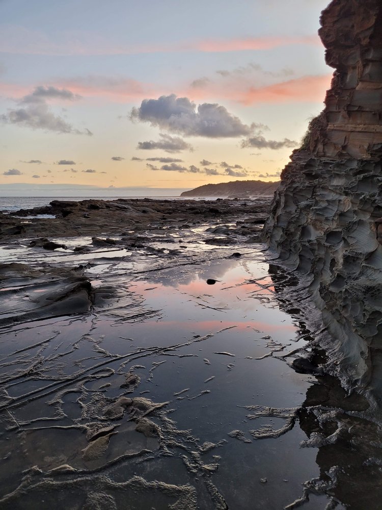 The sky is lit by a sunset, with beautiful colours reflected in the rockpool