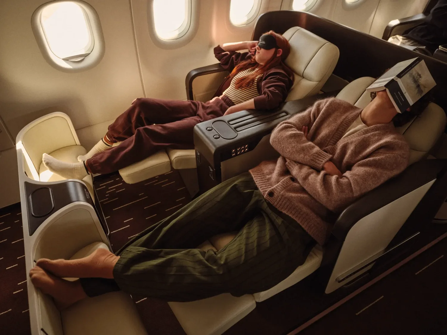 Two guests resting in reclined cream leather seats in the Four Seasons Private Jet cabin