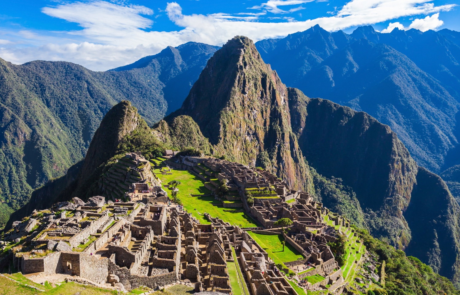The stone terraces and ruins of Machu Picchu below a steep green peak in the Andes