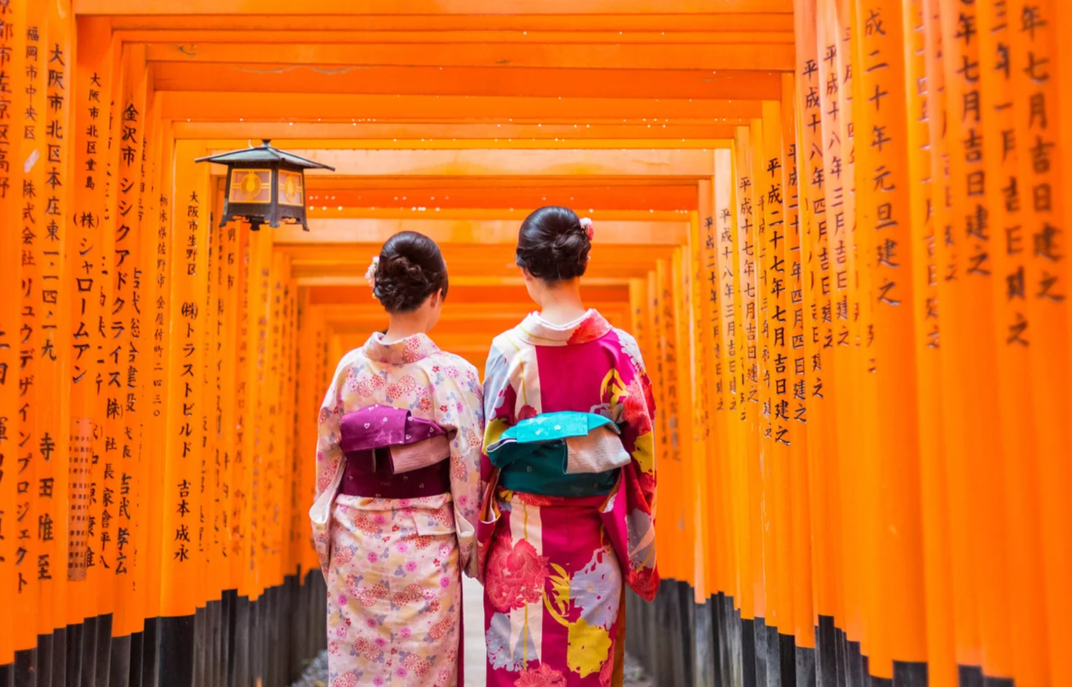 Two women in kimonos walking through a tunnel of vermilion torii gates in Kyoto