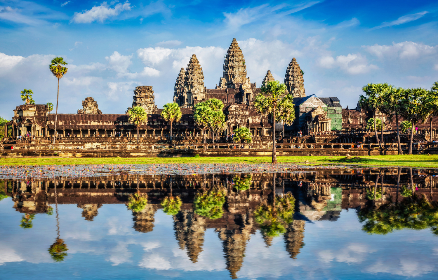 Angkor Wat’s temple towers and palms reflected in a still pond under a blue sky