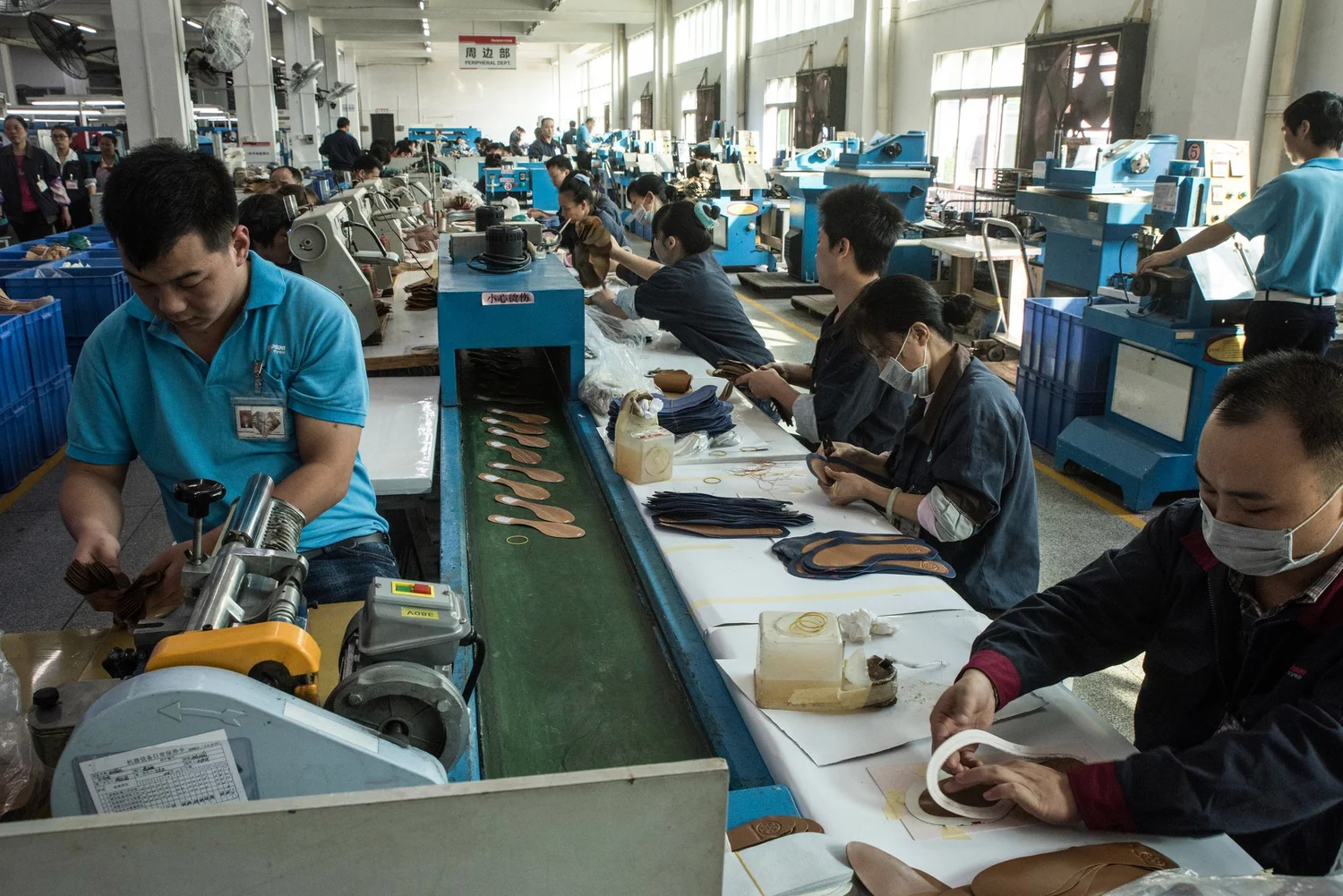 Workers preparing shoe components along a conveyor line at a footwear factory in China