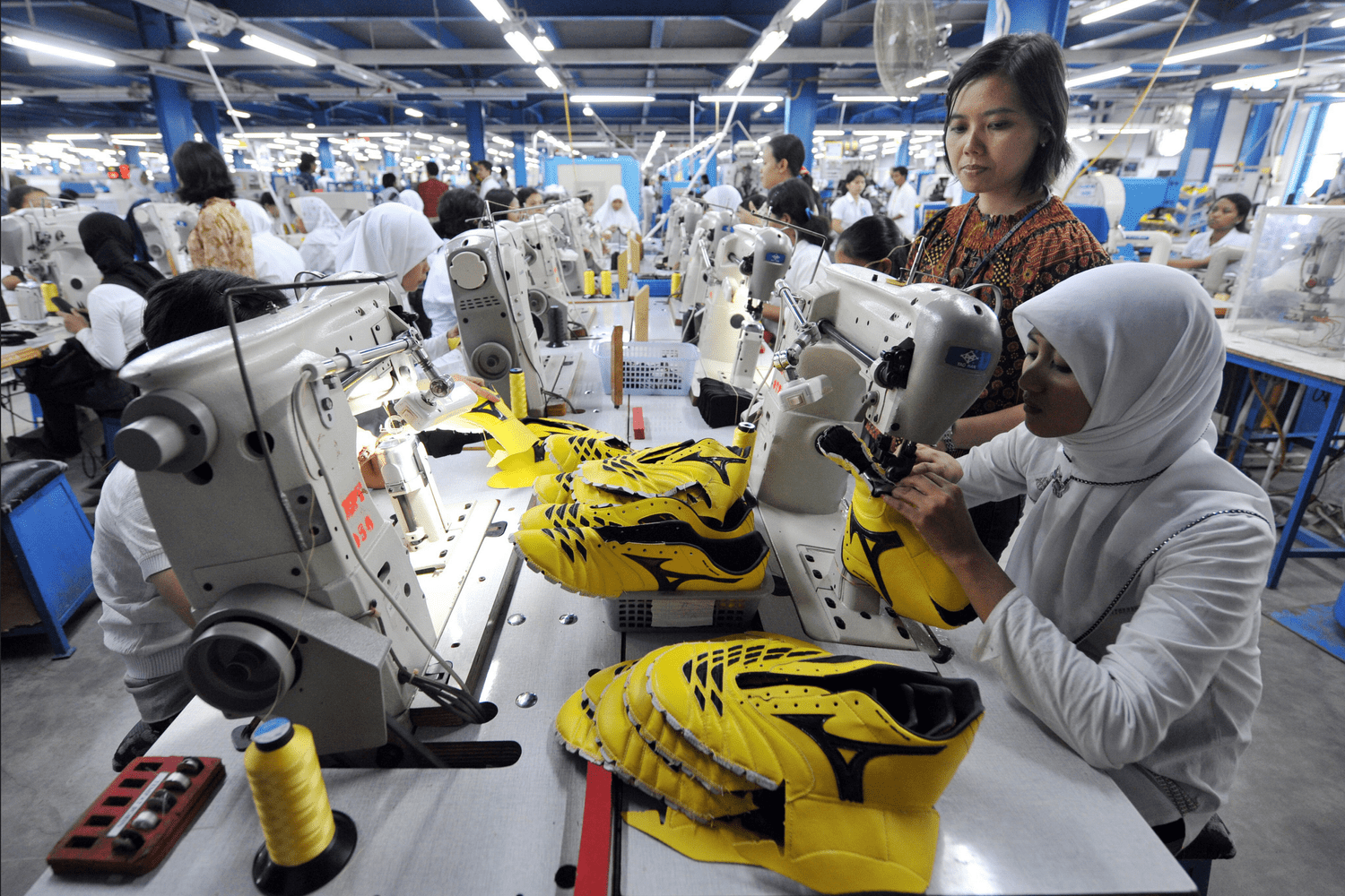 Workers stitching yellow athletic shoe uppers at a large shoe factory in Indonesia