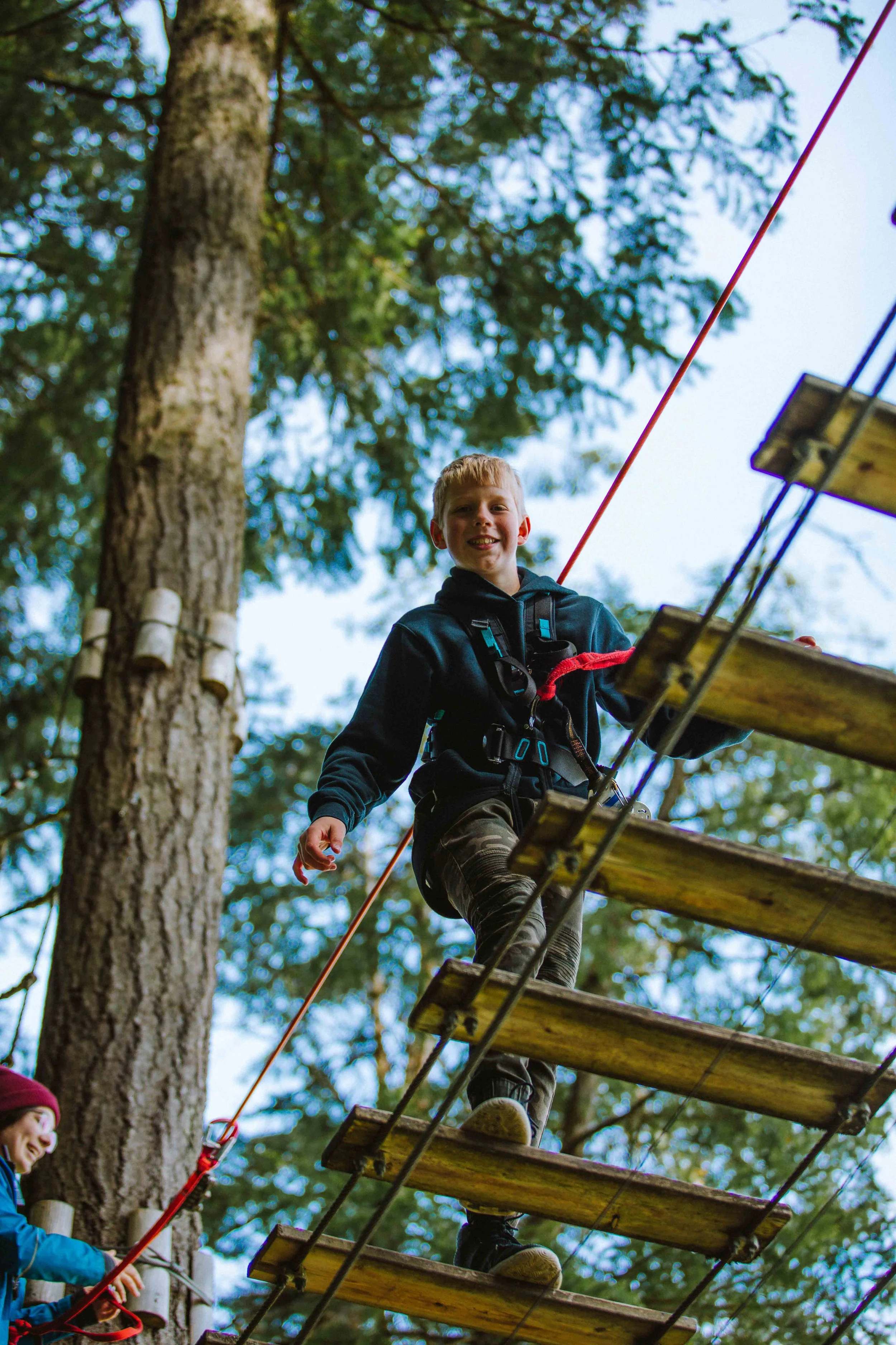 Student balancing across a suspended bridge in the treetops
