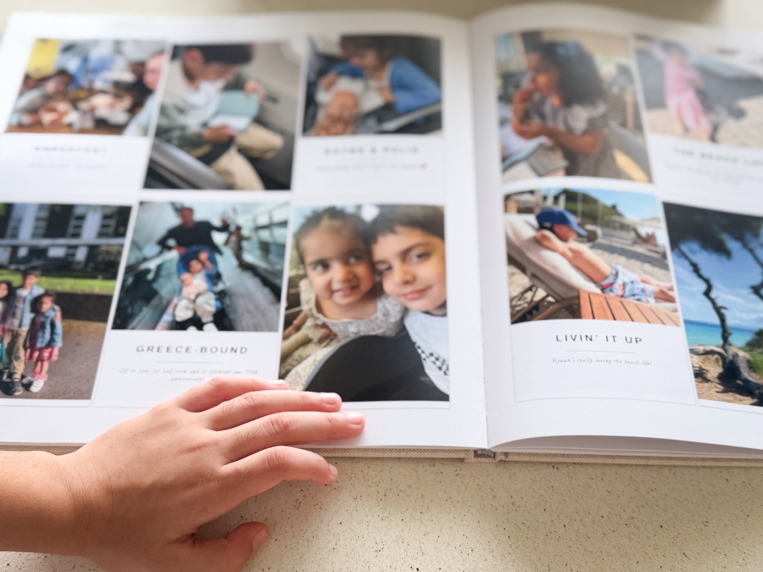 Hands holding open a printed family memory book showing completed photo pages