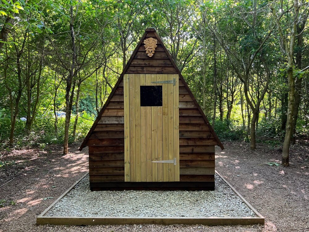 The simple timber Woodland Bolthole shelter surrounded by leafy trees