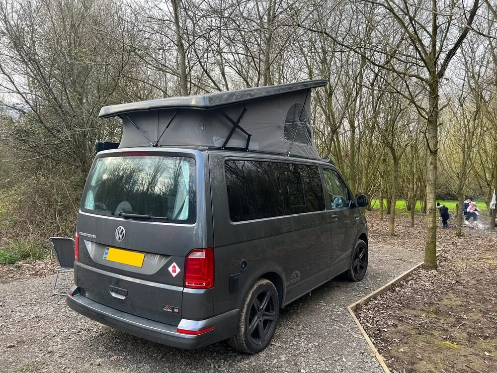 A campervan with its pop-top raised on a Fire & Stars pitch surrounded by trees