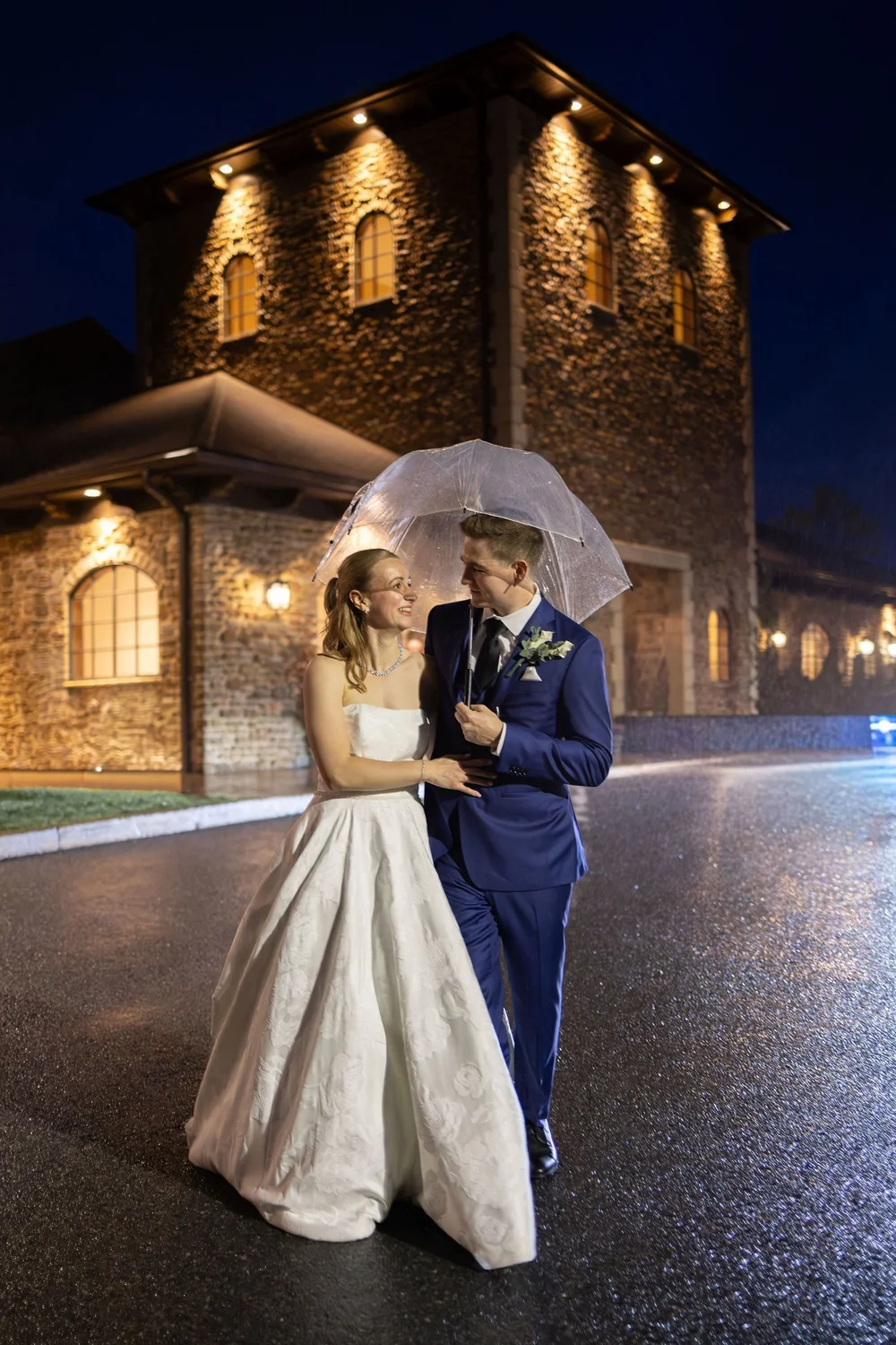 Couple under a clear umbrella outside the lit stone tower at night