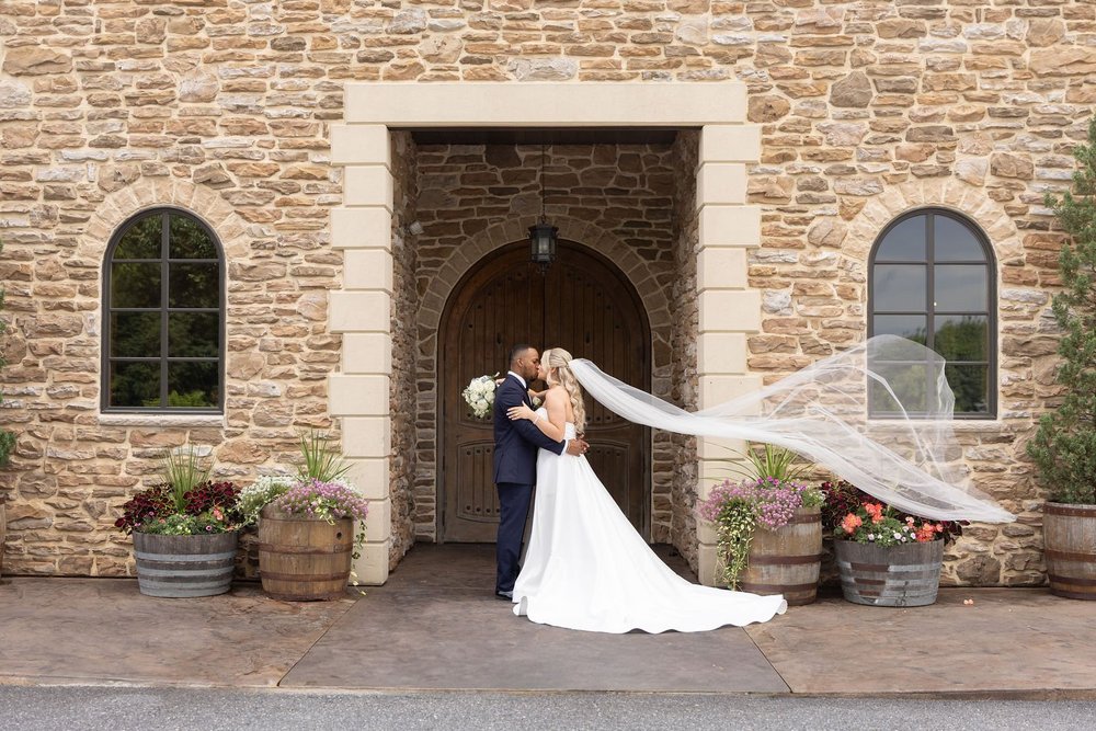 Bride's veil flying in front of the arched wooden doors at Folino Estate