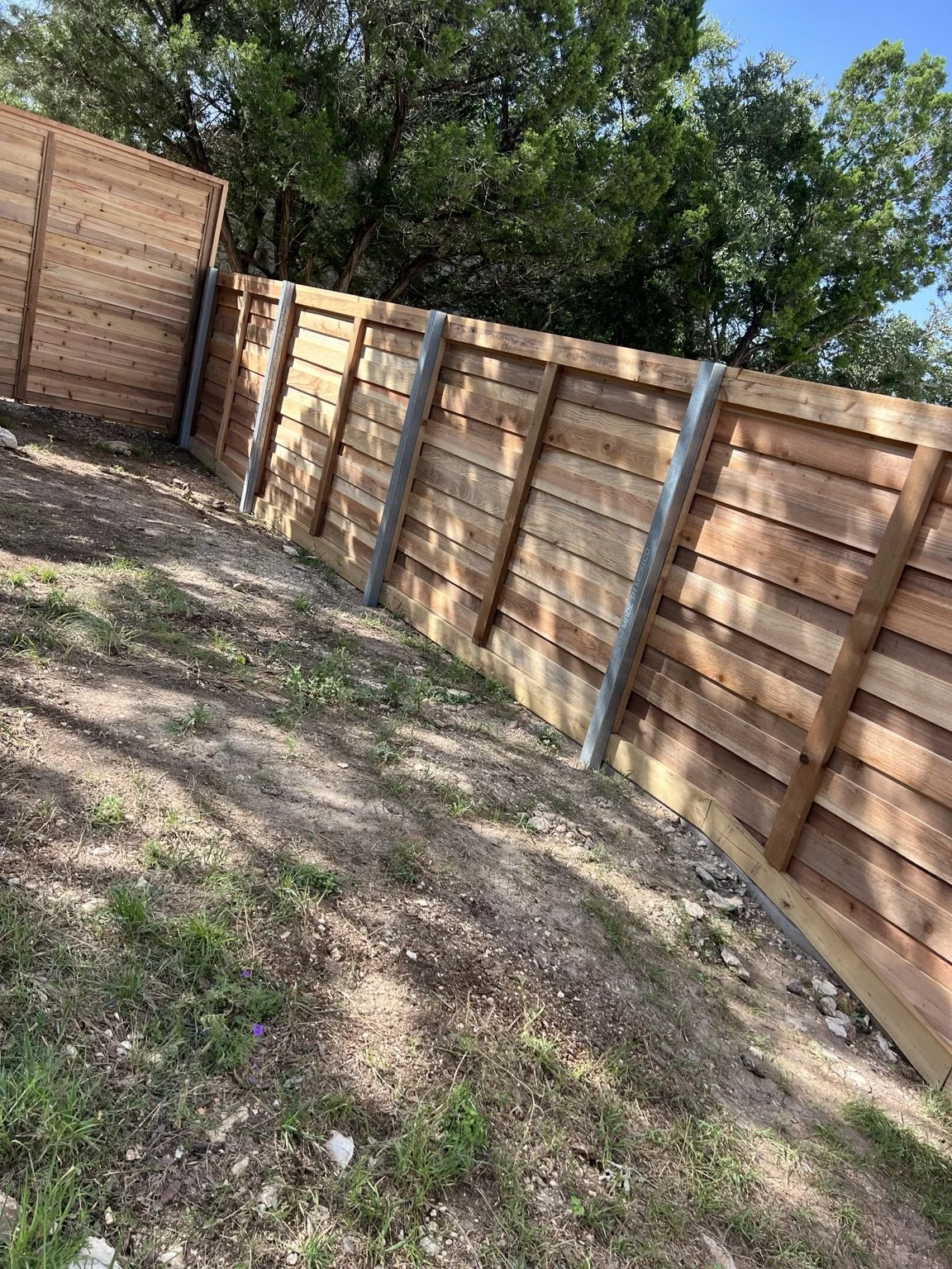 Back of the Timberwood Park cedar fence showing galvanized steel posts on sloping ground