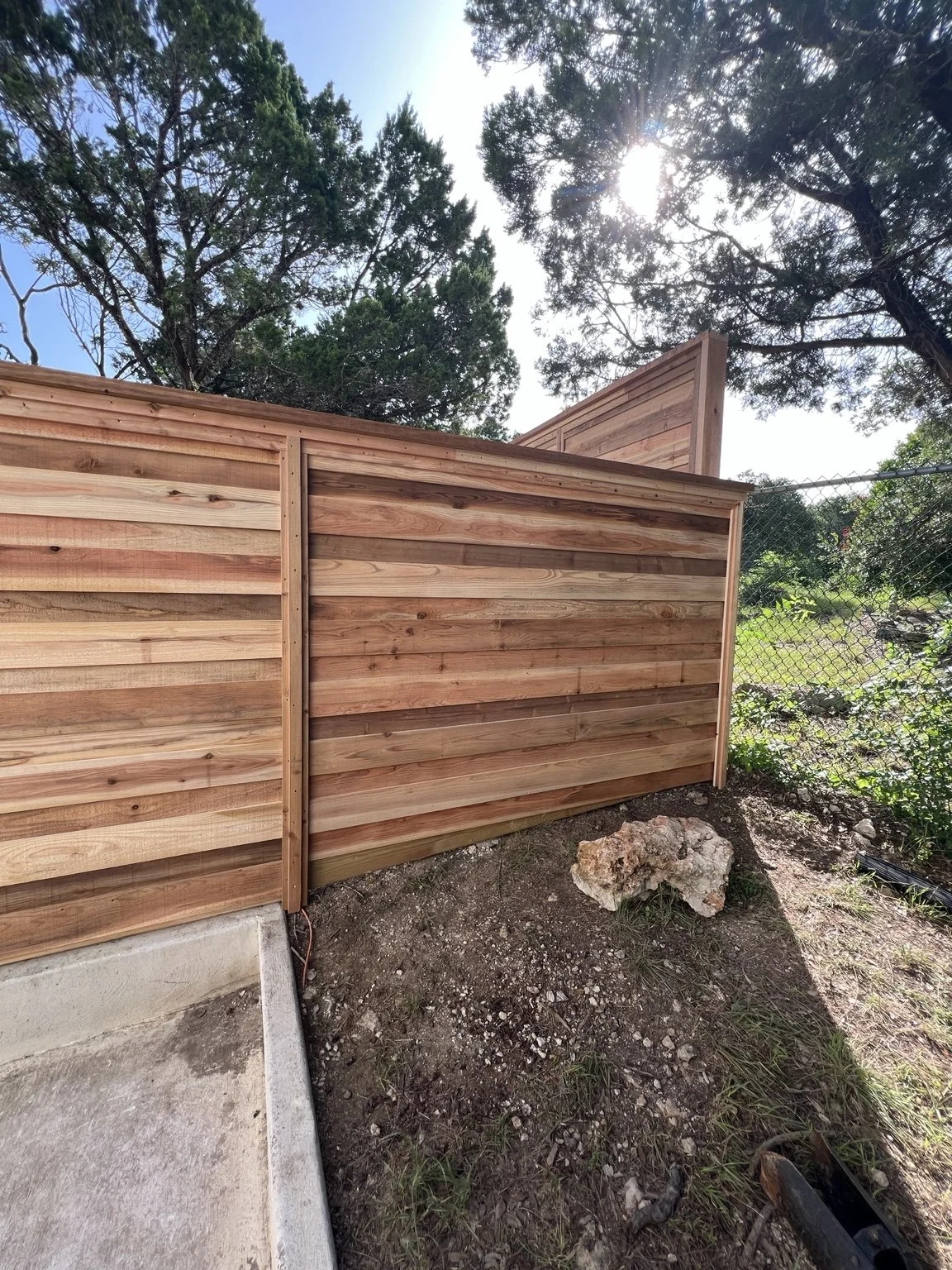 Horizontal cedar fence with cap and trim beside exposed limestone and a change in ground level
