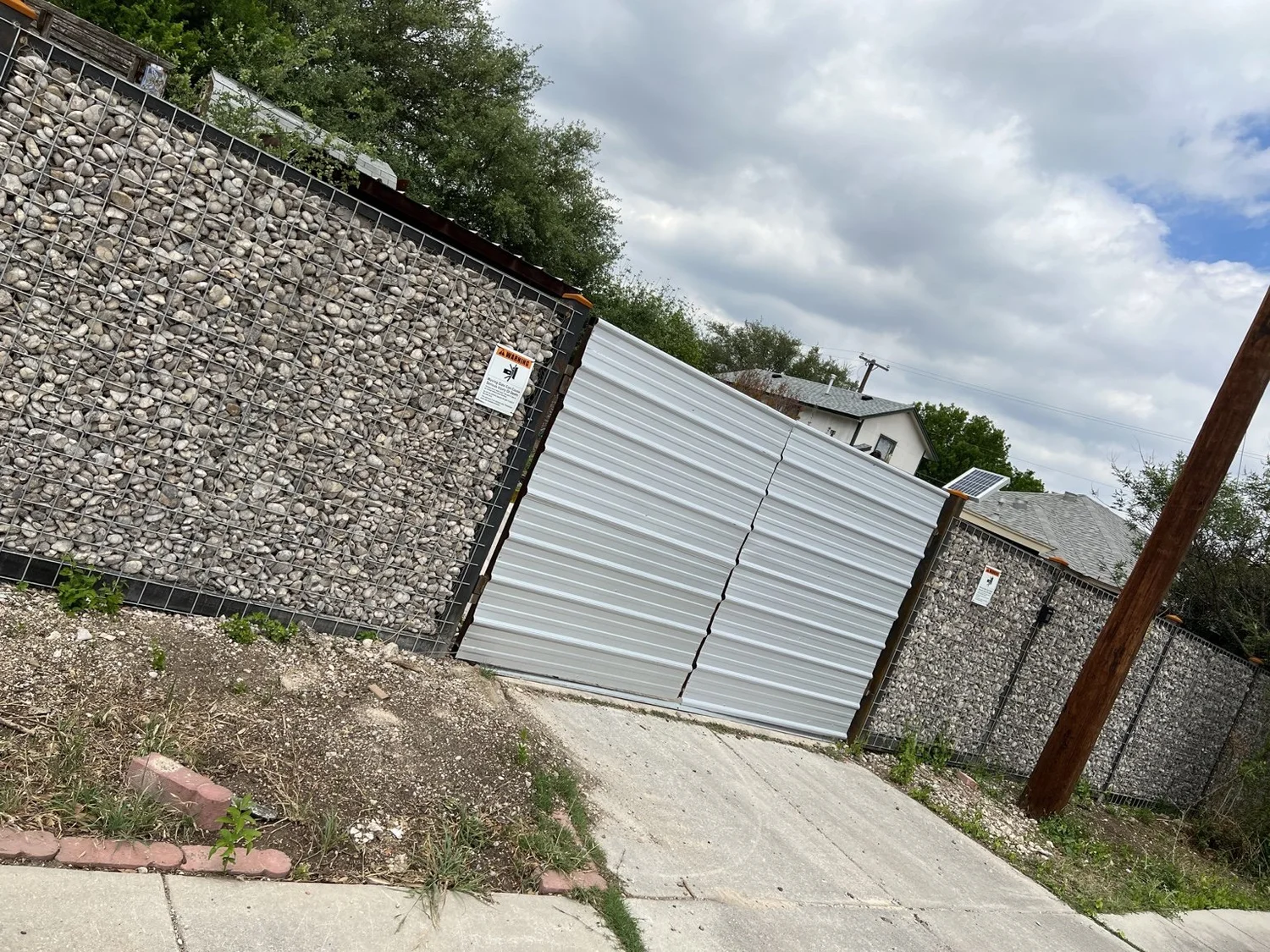 Metal double driveway gates between river-rock gabion fence sections in San Antonio
