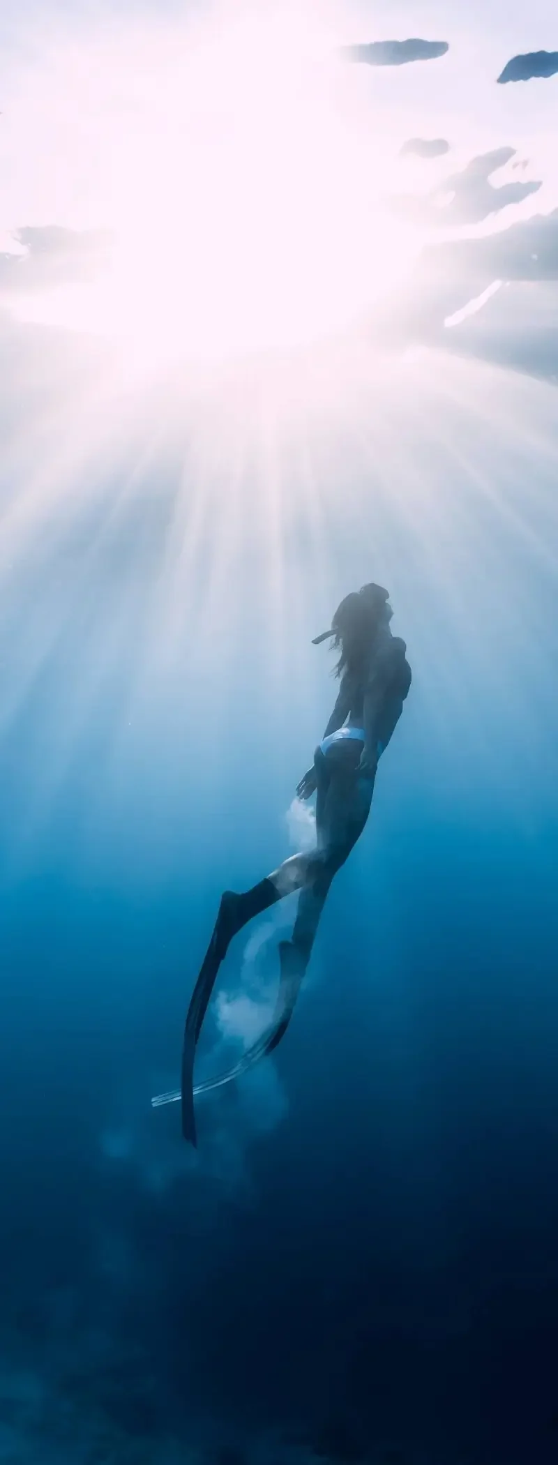A freediver ascending through shafts of light toward the surface